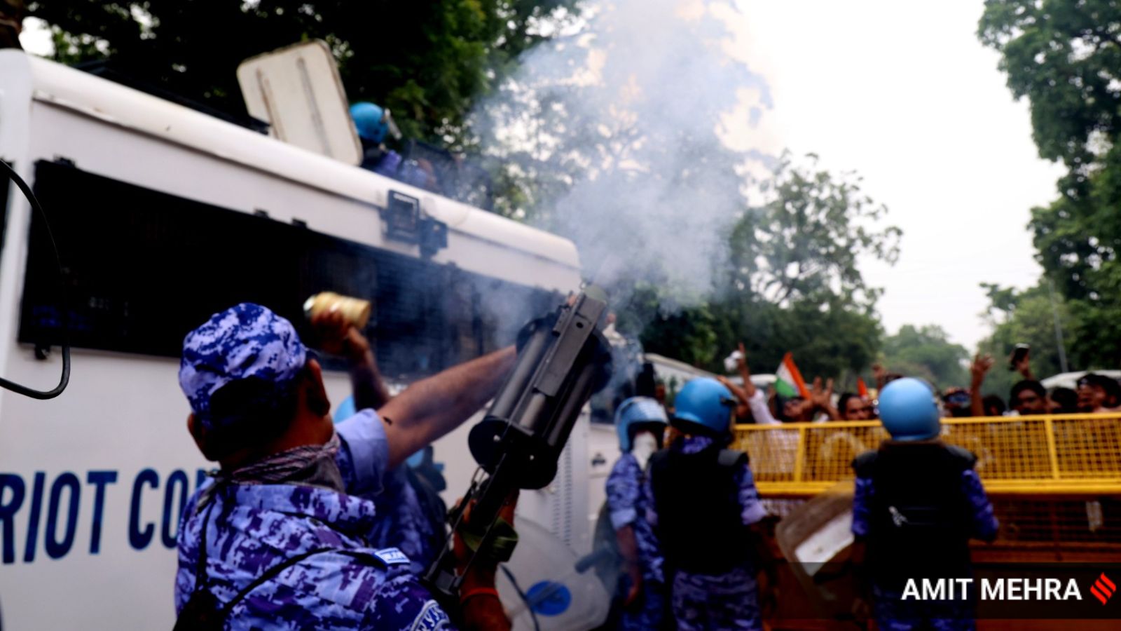 Riot control officer firing a tear gas shell from a launcher toward protesters behind a barricade
